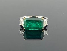 This ring is a simple but elegant with its high quality 4.64 carat emerald stone in the center of the ring cushioned with two trapezoid cut diamonds on its sides. . The Emerald is of Zambian origin an has a beautiful luster and a vivid green color. The stones are set in 18K White Gold with yellow gold prongs securing the emerald. The ring is currently sized at US7, and it can be resized. Gold : 4.34 grams  Diamond Trapezoid: 0.48 Ctw Emerald Oct: 4.64 Ctw Emerald Three Stone Ring, Emerald Ring Design, Three Stone Ring Settings, Stylish People, Diamond Three Stone Ring, Three Stone Diamond Rings Engagement, Beautiful Baubles, Statement Rings Diamond, Ring Settings