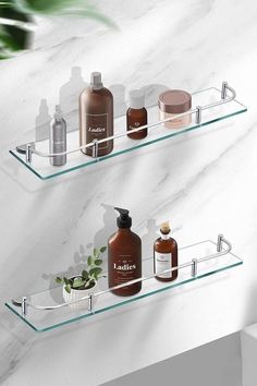 two glass shelves with bottles on them in front of a white marble wall and plant