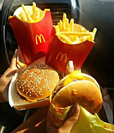 a person holding a plate with two hamburgers and fries