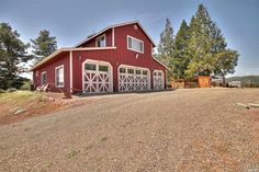 a red barn with two garages on the side and trees in the back ground