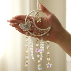 a person's hand holding a white dream catcher with beads and butterflies on it