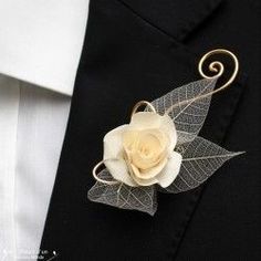 a boutonniere with a white rose and leaf decoration on it's lapel