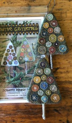 two christmas trees made out of buttons on top of a wooden table