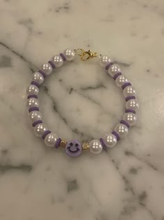 the purple and white beaded bracelet has a smiley face on it