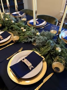 the table is set with blue and gold plates, silverware, greenery and candles