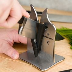 a person is using a knife sharpener on a cutting board with vegetables in the background