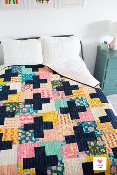 a bed with a quilt on top of it in a bedroom next to a dresser