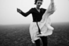 a woman is standing in the middle of an open field with her arms spread out