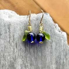 Adorable Alaska Blueberry Earrings! These earrings feature bright cobalt clear blueberries with frosted green leafs wire wrapped in gold. They are proudly handcrafted in Alaska in my original design and are a great gift for anyone who loves fall time and blueberry picking! These bright blueberry earrings would make a great addition to any outfit! * Clear Cobalt Blue Czech Glass Beads for the Berry and Frosted Bright Green Czech Glass Leafs. * Earrings Measure 1 1/2" long x 5/8" wide. * Wire Wrapped to secure leaf permanently. * Handmade Gold Tone Ear Wires (Brass). * Free Shipping to the US. * Ships within 1-3 business days via USPS First Class mail and tracking info when shipped. For more Alaskan Inspired gifts from this artist visit:  907northdesigns.etsy.com Blue Glass Wire Wrapped Earrings, Blue Wire Wrapped Glass Earrings, Blue Wire-wrapped Glass Earrings, Blue Nickel-free Recycled Glass Earrings, Nickel-free Blue Recycled Glass Earrings, Blue Teardrop Recycled Glass Jewelry, Blue Recycled Glass Nickel-free Earrings, Blue Recycled Glass Dangle Earrings, Nickel-free Blue Recycled Glass Jewelry