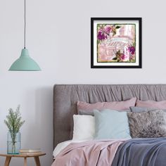 a bed with pink sheets and pillows next to a wall mounted art print on the wall