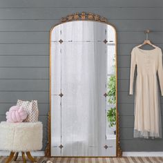 a dress hanging on a wall next to a mirror and stool with a teddy bear