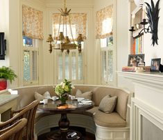 a corner table with two chairs and a bench in front of the window that is decorated with flowers