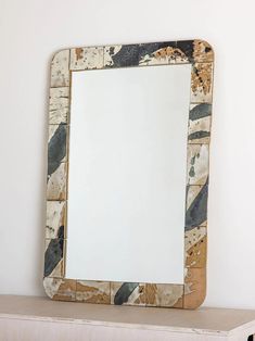 a mirror sitting on top of a wooden shelf next to a white wall with black and brown designs