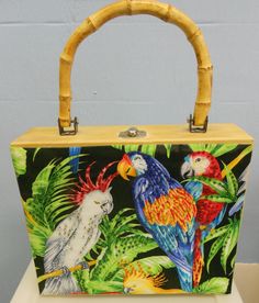 a handbag with parrots painted on it and bamboo handles, sitting on a table