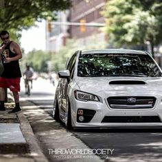 a white subarunt is parked on the side of the street with a man standing next to it