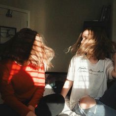 two young women sitting on the floor with their hair blowing in the wind and sunlight shining through them