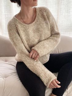 a woman sitting on top of a white couch wearing black pants and a sweater over her shoulders