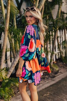 - Embrace floral vibes with this flowy dress! - Soft material with a pink, red, orange, yellow, blue, and green hued floral print - A built-in lining - A v-cut neckline with a tie detail - Long, loose sleeves with elastic cuffs - A lightweight silhouette that ends in a mini dress length hemline Multicolor V-neck Floral Dress With Vibrant Print, Multicolor Print V-neck Summer Dress, Colorful Floral Print V-neck Dress, Colorful V-neck Vacation Dress, Flowy Tropical V-neck Dress, Flowy V-neck Tropical Dress, Multicolor Floral Dress With Vibrant Print For Day Out, Multicolor V-neck Mini Dress With Vibrant Print, Multicolor Floral V-neck Dress With Vibrant Print