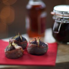 three figs on a red napkin next to jars of honey and jam in the background