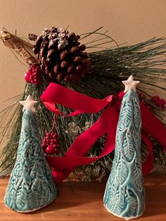 two blue christmas trees with red ribbons and pine cones on the top one is made out of clay