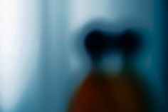 blurry photograph of an orange vase in front of a white curtain with blue trim