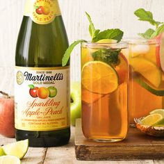 a bottle of sparkling apple punch next to two glasses filled with apples and limes