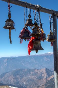 bells hanging from the side of a metal pole on top of a mountain with mountains in the background