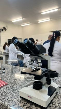 a microscope sitting on top of a counter next to people in white lab coats behind it