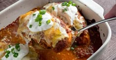 a white dish filled with lasagna covered in sauce and sour cream, topped with green onions