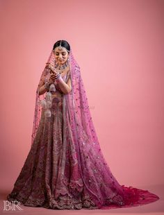 a woman in a pink and gold lehenga poses for the camera with her hands on her hips