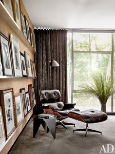 an eames chair and ottoman in front of a large window with pictures on the wall