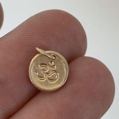 A tiny pendant with a texture like stone and an om or ohm symbol. The pendant measures about a quarter of an inch or slightly larger and is made of solid 14k yellow gold. Also available without the om symbol. A plain pebble pendant is shown modeled on a 16" chain for size reference; chain is not included. Made to order within 3-5 days.See here for more photos: http://www.etsy.com/listing/34030666/tiny-14k-gold-pebble-necklaceIMPORTANT: Please be aware that delivery times are estimates and USPS m Symbolic Yellow Gold Brass Charms, Spiritual 14k Gold Charm Necklaces With Coin Pendant, Spiritual 14k Gold Charm Necklace With Round Pendant, 14k Gold Spiritual Round Pendant Charm Necklace, Symbolic Yellow Gold Charms With Round Pendant, Symbolic Yellow Gold Round Pendant Charms, Symbolic Engraved Yellow Gold Charms, Symbolic 14k Gold Engraved Charm Necklaces, Yellow Gold Symbolic Charms For Good Luck