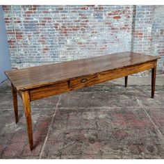 an old wooden table with two drawers in front of a brick wall and stone floor