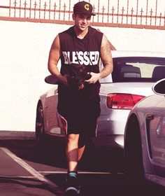 a man in a tank top and skirt walking down the street with his dog wearing a hat