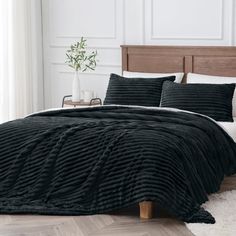 a bed with black comforter and pillows in a white room next to a wooden headboard