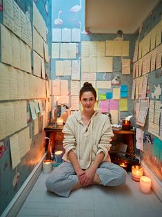 a woman sitting on the floor in front of a wall full of notes and candles