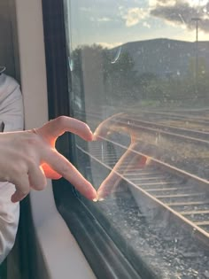 a person making a heart with their hands while looking out the window at train tracks