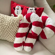 two red and white striped christmas pillows on a couch with snowmen in the background