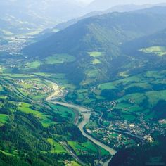 an aerial view of a river running through a valley surrounded by green fields and mountains