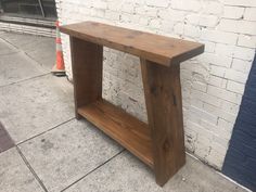 a wooden bench sitting on the side of a road next to a brick wall and sidewalk