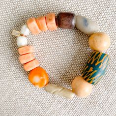 Sustainable Bracelet. A bright bold green hand painted prayer bead with neutral rosewood and soft peach beads. African prayer beads from Africa’s Ivory Coast for loyalty, love and health. Featuires orange coral stone. Rosewood from the tree of health and wisdom. Freshwater large pearls in mint. Sterling silver BelleStyle logo tag. Comes in linen travel pouch. One of a kind. Made in USA. Spiritual Wooden Beads Stretch Bracelet For Healing, Artisan Wooden Beads Bracelet For Meditation, Artisan Wooden Beads Bracelets For Meditation, Handmade Orange Beaded Bracelets For Meditation, Handmade Spiritual Orange Stretch Bracelet, Earthy Wooden Beaded Bracelets For Gift, Earthy Wooden Beaded Bracelets As Gift, Orange Bohemian Beaded Bracelets With 8mm Beads, Artisan Orange Bracelet With Colorful Beads