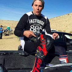 a man sitting in the back of a pick up truck holding a snowboard and helmet