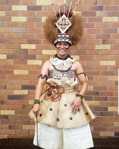 a woman with an afro standing in front of a brick wall wearing a dress and headdress