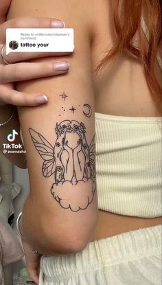 a woman's arm with a tattoo on it and an angel sitting on the cloud