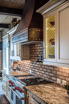 a kitchen with white cabinets and marble counter tops, an oven hood over the stove