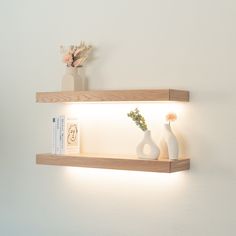 two white vases are sitting on a shelf next to a book and some flowers