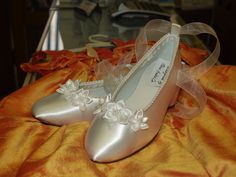 a pair of silver shoes with white flowers on the heel and ribbon around the toe