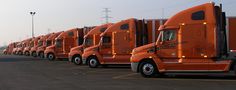 a row of orange semi trucks parked in a parking lot