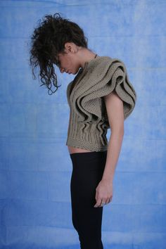 a woman standing in front of a blue backdrop wearing a sweater and leggings