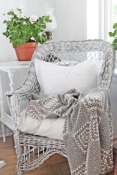 a wicker chair with white pillows and a blanket on top of it next to a potted plant